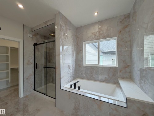 Bathroom featuring a built-in soaking tub with matte black fixtures, a window, a glass-enclosed shower with matte black framing, and large-format tile walls and flooring - 202 Edgewater Circle, Leduc, AB - Indoor Photo Showing Bathroom