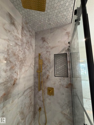 Shower enclosure featuring large format stone-look tile, honeycomb tile ceiling, recessed niche with honeycomb tile, gold-finish shower fixtures, and a frameless glass door with black trim - 202 Edgewater Circle, Leduc, AB - Indoor Photo Showing Bathroom