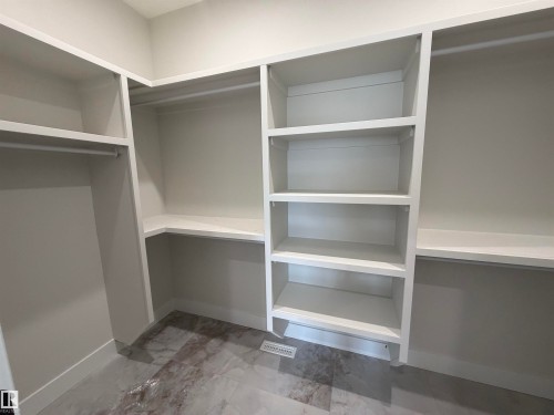 Walk-in closet featuring built-in white shelving, hanging rods, and a marble-finish tile floor - 202 Edgewater Circle, Leduc, AB - Indoor With Storage