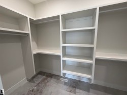 Walk-in closet featuring built-in white shelving, hanging rods, and a marble-finish tile floor - 