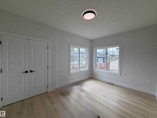Spacious room featuring light wood-finish flooring, dual panel doors with matte black hardware, and two large windows offering ample natural light - 202 Edgewater Circle, Leduc, AB - Indoor Photo Showing Other Room