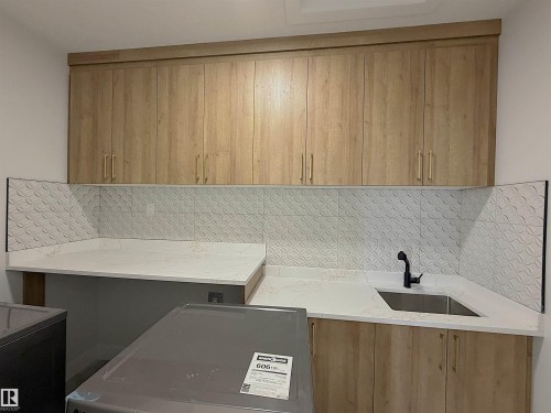 Laundry area featuring light wood-finish cabinetry, white countertops, and a textured backsplash - 202 Edgewater Circle, Leduc, AB - Indoor Photo Showing Kitchen
