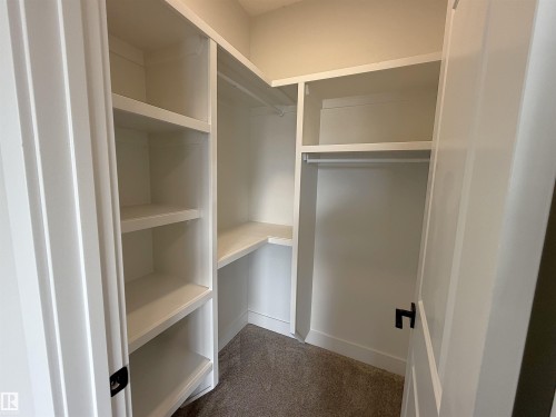Walk-in closet featuring built-in shelving, hanging rods, an integrated corner shelf, and carpet flooring - 202 Edgewater Circle, Leduc, AB - Indoor With Storage