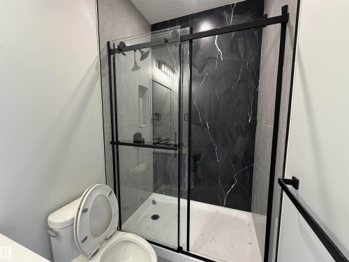 Contemporary shower enclosure featuring black-framed sliding glass doors, white shower pan, and dramatic black marble-look tile - 202 Edgewater Circle, Leduc, AB - Indoor Photo Showing Bathroom