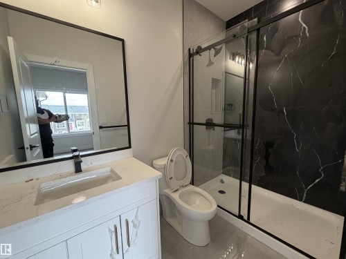 Contemporary bathroom featuring a white vanity with a quartz-finish countertop and an integrated sink, a black-framed mirror, a black-framed glass shower enclosure, and dark marble-look shower wall tiling - 202 Edgewater Circle, Leduc, AB - Indoor Photo Showing Bathroom