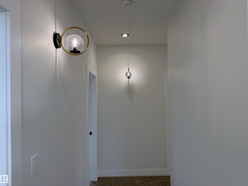 Hallway featuring contemporary wall sconces, recessed ceiling lighting, light neutral wall paint, white baseboards, and a framed doorway - 202 Edgewater Circle, Leduc, AB - Indoor Photo Showing Other Room