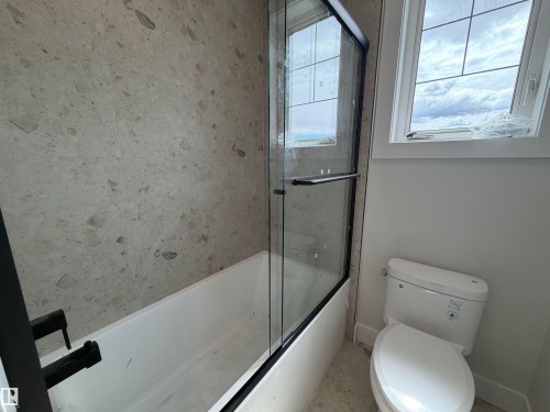 Bathroom featuring a white bathtub with a black-framed glass shower enclosure, a full wall of patterned tile, and a white toilet - 202 Edgewater Circle, Leduc, AB - Indoor Photo Showing Bathroom