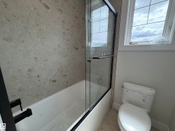 Bathroom featuring a white bathtub with a black-framed glass shower enclosure, a full wall of patterned tile, and a white toilet - 