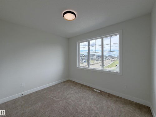 Bright interior space featuring a multi-pane window, neutral-toned carpeting, white baseboards, and a contemporary flush-mount ceiling light fixture - 202 Edgewater Circle, Leduc, AB - Indoor Photo Showing Other Room