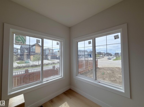 Bright interior space featuring two large windows with white trim, grid patterns, and light wood-finish flooring - 202 Edgewater Circle, Leduc, AB - Indoor Photo Showing Other Room