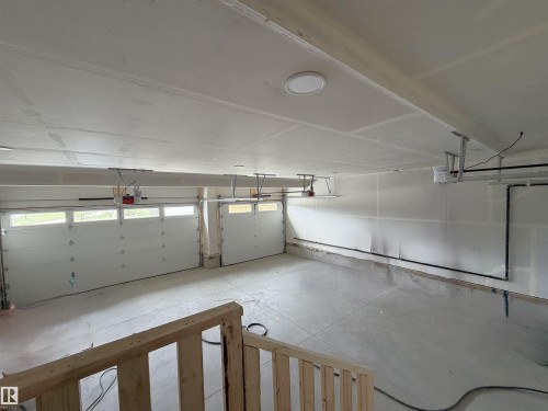 Spacious 4-car garage featuring white paneled overhead doors with window inserts, concrete flooring, and ceiling-mounted lighting - 202 Edgewater Circle, Leduc, AB - Indoor Photo Showing Garage