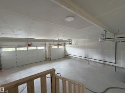 Spacious 4-car garage featuring white paneled overhead doors with window inserts, concrete flooring, and ceiling-mounted lighting - 