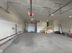 Spacious garage featuring concrete flooring, unpainted drywall, exposed metal garage door tracks, and recessed ceiling lighting - 