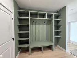 Built-in sage green mudroom bench with beadboard backing, integrated shelving, and coat hooks - 