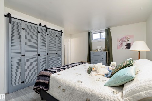 Louvered bi-fold doors with black hardware, plank-style flooring, a window with exterior visibility, and white walls - 17 Camelot Avenue, Leduc, AB - Indoor Photo Showing Bedroom