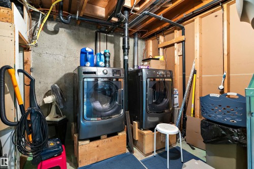 Dedicated laundry area featuring a front-loading washer and dryer set, concrete wall, and exposed wood framing - 17 Camelot Avenue, Leduc, AB - Indoor Photo Showing Laundry Room