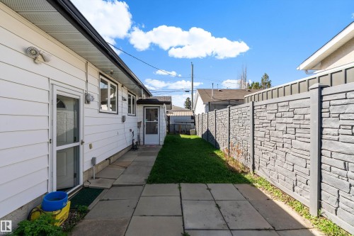 Side yard featuring a concrete paver path, a manicured lawn strip, and a textured stone-look privacy fence - 17 Camelot Avenue, Leduc, AB - Outdoor With Exterior