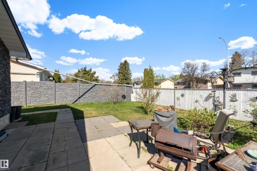 Expansive backyard featuring a stone-look block fence, a white picket fence, mature trees, and a paved patio area - 17 Camelot Avenue, Leduc, AB - Outdoor