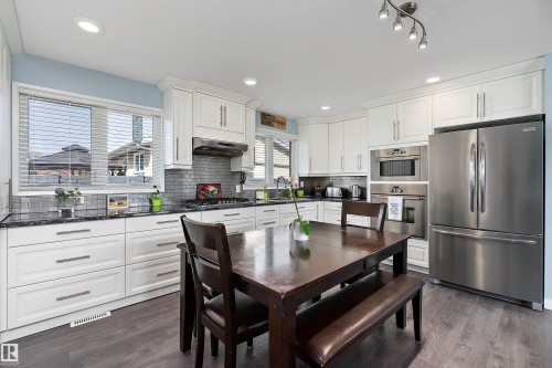Bright kitchen featuring white cabinetry, a subway tile backsplash, dark granite countertops, stainless steel appliances, and wood-finish flooring - 17 Camelot Avenue, Leduc, AB - Indoor Photo Showing Kitchen With Upgraded Kitchen