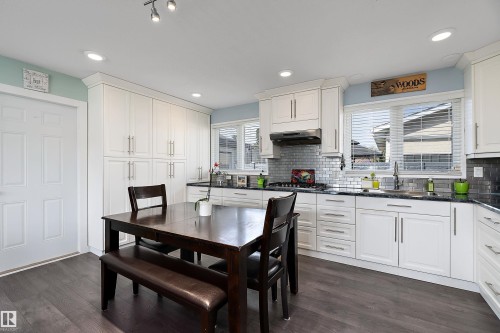Modern kitchen featuring extensive white cabinetry, dark wood-finish flooring, recessed lighting, a stainless steel range hood, and a subway tile backsplash - 17 Camelot Avenue, Leduc, AB - Indoor