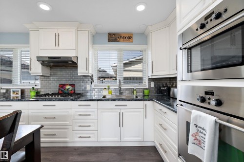 Kitchen featuring white cabinetry with brushed nickel hardware, a subway tile backsplash, dark countertops, and stainless steel built-in appliances - 17 Camelot Avenue, Leduc, AB - Indoor Photo Showing Kitchen With Upgraded Kitchen