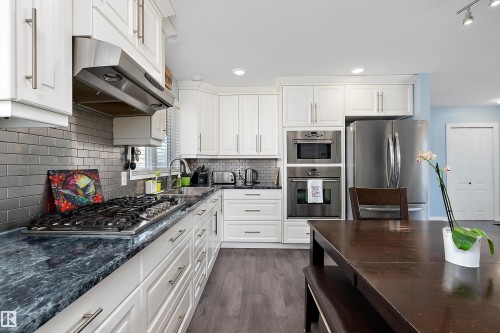 Kitchen with white cabinetry, dark marbled countertops, and a stainless steel appliance package, including a gas range with hood vent and built-in double oven - 17 Camelot Avenue, Leduc, AB - Indoor Photo Showing Kitchen With Upgraded Kitchen
