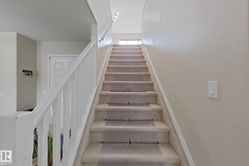 The property features an interior stairway with a carpeted runner and white risers, complemented by white railings and neutral-toned walls - 3120 25 Avenue Nw, Edmonton, AB - Indoor Photo Showing Other Room