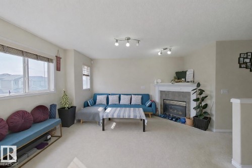 The living area features light-colored carpeting, large windows providing natural light, and a fireplace with a mantel - 3120 25 Avenue Nw, Edmonton, AB - Indoor With Fireplace