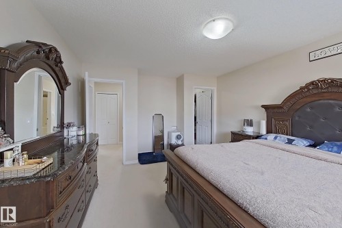 The bedroom offers light-colored walls and carpeted flooring, featuring a decorative dark wood dresser with a mirror, and a matching bed frame with an upholstered headboard - 3120 25 Avenue Nw, Edmonton, AB - Indoor Photo Showing Bedroom