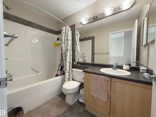Bathroom featuring a bathtub and shower combination, a vanity with a dark countertop and light wood cabinetry, and a large mirror with overhead lighting - 3120 25 Avenue Nw, Edmonton, AB - Indoor Photo Showing Bathroom