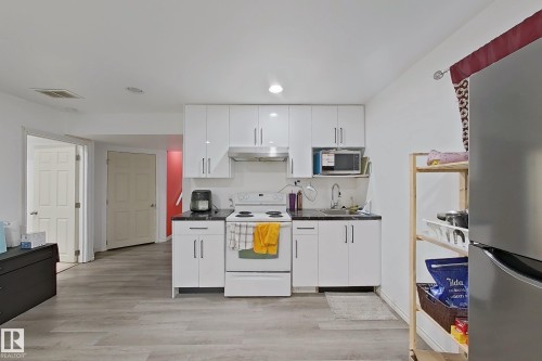 Kitchen area featuring white cabinetry, a white stove, a stainless steel microwave, and a stainless steel refrigerator - 3120 25 Avenue Nw, Edmonton, AB - Indoor Photo Showing Kitchen