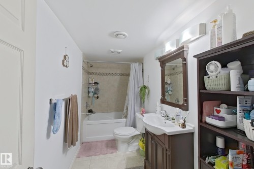 The bathroom features a bathtub with a tiled shower surround, a toilet, and a vanity with an integrated sink and mirror - 3120 25 Avenue Nw, Edmonton, AB - Indoor Photo Showing Bathroom