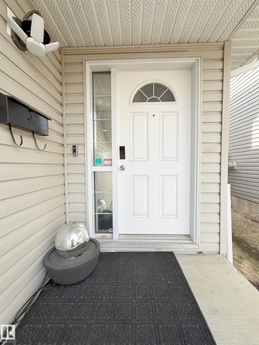 The property features a front door with an arched transom window and a sidelight, set within a light-colored siding exterior - 3120 25 Avenue Nw, Edmonton, AB - Outdoor With Exterior