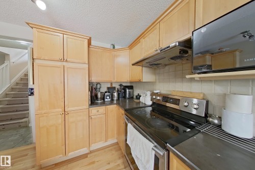The kitchen features light wood cabinetry, dark countertops, a stainless steel range, and a tiled backsplash - 3120 25 Avenue Nw, Edmonton, AB - Indoor Photo Showing Kitchen