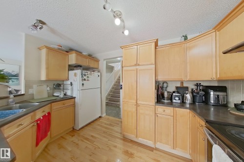 Kitchen featuring light wood cabinetry, a white refrigerator, a stainless steel sink, and dark countertops - 3120 25 Avenue Nw, Edmonton, AB - Indoor Photo Showing Kitchen