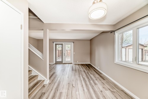 Spacious interior featuring wood-finish flooring, a contemporary ceiling light fixture, a large window with ample natural light, and double glass doors providing exterior access - 2578 138A Avenue, Edmonton, AB - Indoor Photo Showing Other Room
