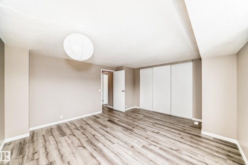Spacious room featuring wood-finish flooring, neutral-toned walls, a white paper lantern light fixture, and floor-to-ceiling sliding closet doors - 2578 138A Avenue, Edmonton, AB - Indoor Photo Showing Other Room