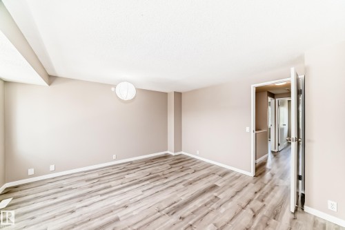 Spacious room featuring wood-finish flooring, light neutral wall paint, white baseboards, and a contemporary wall-mounted light fixture - 2578 138A Avenue, Edmonton, AB - Indoor Photo Showing Other Room
