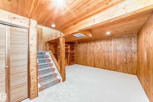 Finished room featuring extensive wood paneling, wood plank ceiling, light-toned carpeting, built-in shelving, and a carpeted staircase - 2578 138A Avenue, Edmonton, AB - Indoor Photo Showing Other Room