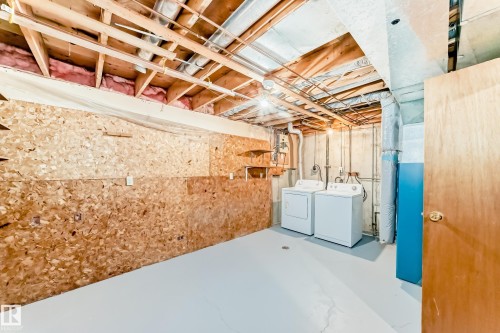 Unfinished basement space featuring exposed wood joists and subfloor, a wood-finish interior door, and a painted concrete floor - 2578 138A Avenue, Edmonton, AB - Indoor Photo Showing Laundry Room