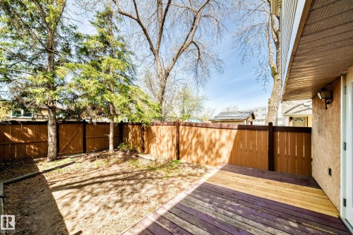 Outdoor deck area featuring wood-finish decking, privacy fencing, mature trees, and exterior wall lighting - 2578 138A Avenue, Edmonton, AB - Outdoor