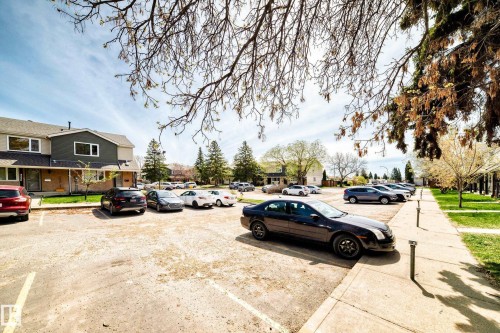 Paved parking area featuring multiple designated parking spaces, concrete sidewalks, and a row of townhome-style residences with dark siding and light trim - 2578 138A Avenue, Edmonton, AB - Outdoor