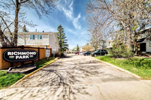 Paved community entrance with a prominent "Richmond Park" sign, bordered by mature trees and manicured lawns - 2578 138A Avenue, Edmonton, AB - Outdoor