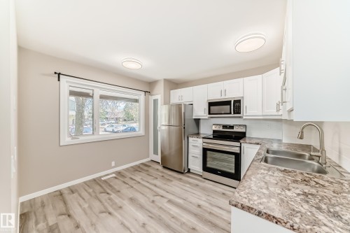 Modern kitchen featuring white cabinetry, stainless steel appliances, wood-finish flooring, and a double basin sink - 2578 138A Avenue, Edmonton, AB - Indoor Photo Showing Kitchen With Double Sink