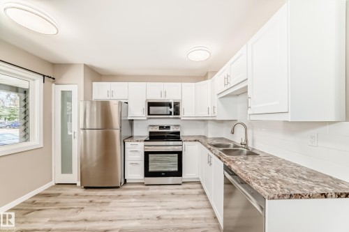 Bright kitchen featuring white cabinetry, stone-finish countertops, and stainless steel appliances - 2578 138A Avenue, Edmonton, AB - Indoor Photo Showing Kitchen With Double Sink