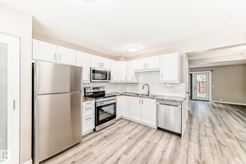 Kitchen featuring white cabinetry, stainless steel appliances, stone-finish countertops, subway tile backsplash, and wood-finish flooring - 2578 138A Avenue, Edmonton, AB - Indoor Photo Showing Kitchen With Double Sink