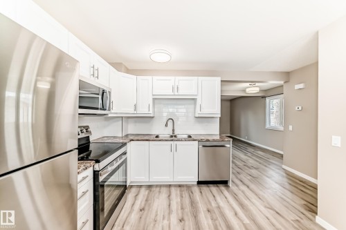 Kitchen featuring white cabinetry, stone-finish countertops, stainless steel appliances, a subway tile backsplash, and wood-finish flooring - 2578 138A Avenue, Edmonton, AB - Indoor Photo Showing Kitchen With Double Sink