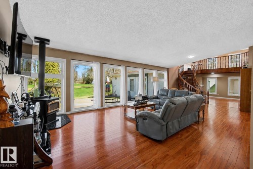 Spacious interior featuring wood-finish flooring, a spiral staircase with wood railing, and a black wood-burning stove on a dark stone hearth - 250 197 Avenue, Edmonton, AB - Indoor Photo Showing Living Room