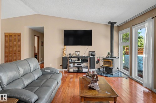 Living area featuring wood-finish flooring, a vaulted ceiling, and a wood-burning stove with a stone-look hearth - 250 197 Avenue, Edmonton, AB - Indoor Photo Showing Living Room With Fireplace