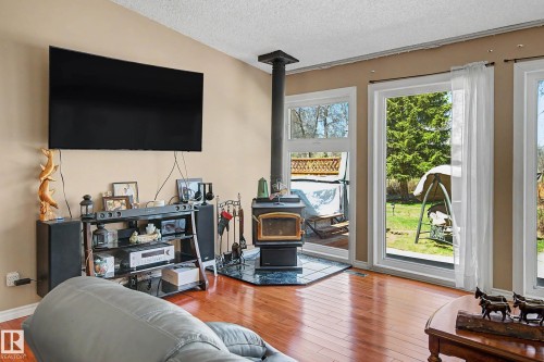 Living area featuring wood-finish flooring, a freestanding wood-burning stove on a dark tile hearth, and multiple large windows with white trim - 250 197 Avenue, Edmonton, AB - Indoor Photo Showing Living Room